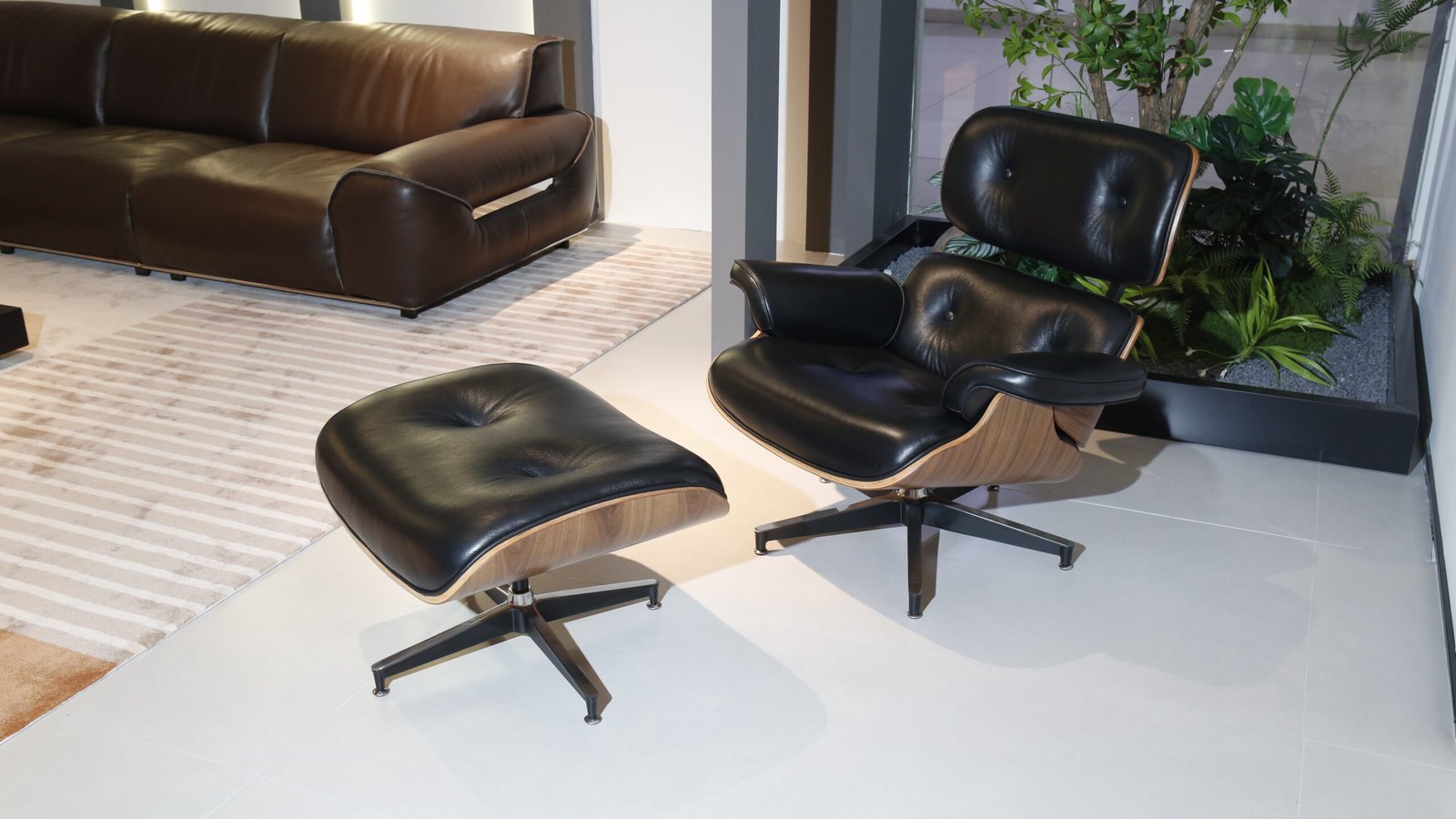 A black leather tufted lounge chair and matching ottoman with walnut shell and star base on a white tile floor